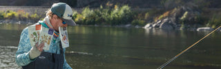 A person stands in the bow of a boat in fishing gear, holding packets of Patagonia Provisions food